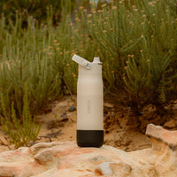 Beige BRITA LARQ water bottle with black silicone boot standing on a stone with nature background.