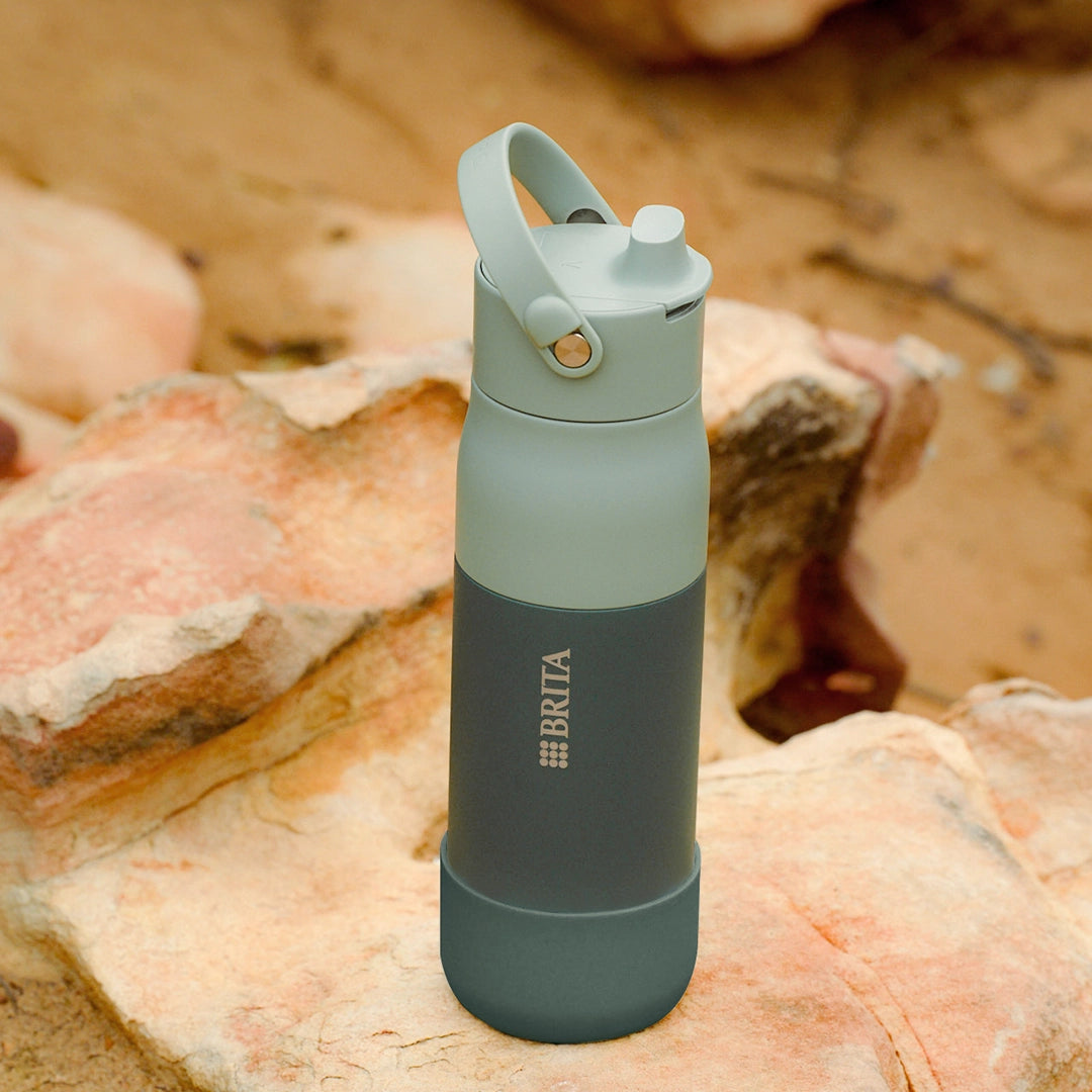 Green BRITA LARQ water bottle with green silicone boot on a stone.